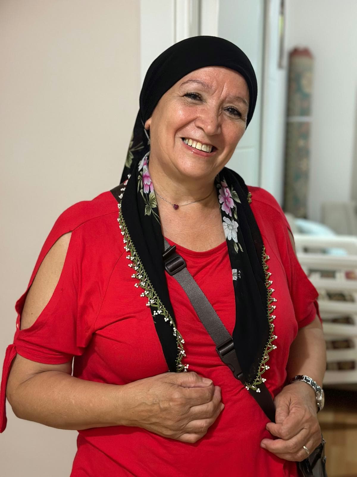 Portret van Naïma Alou Issa, glimlachend, met zwarte hoofddoek en rode blouse